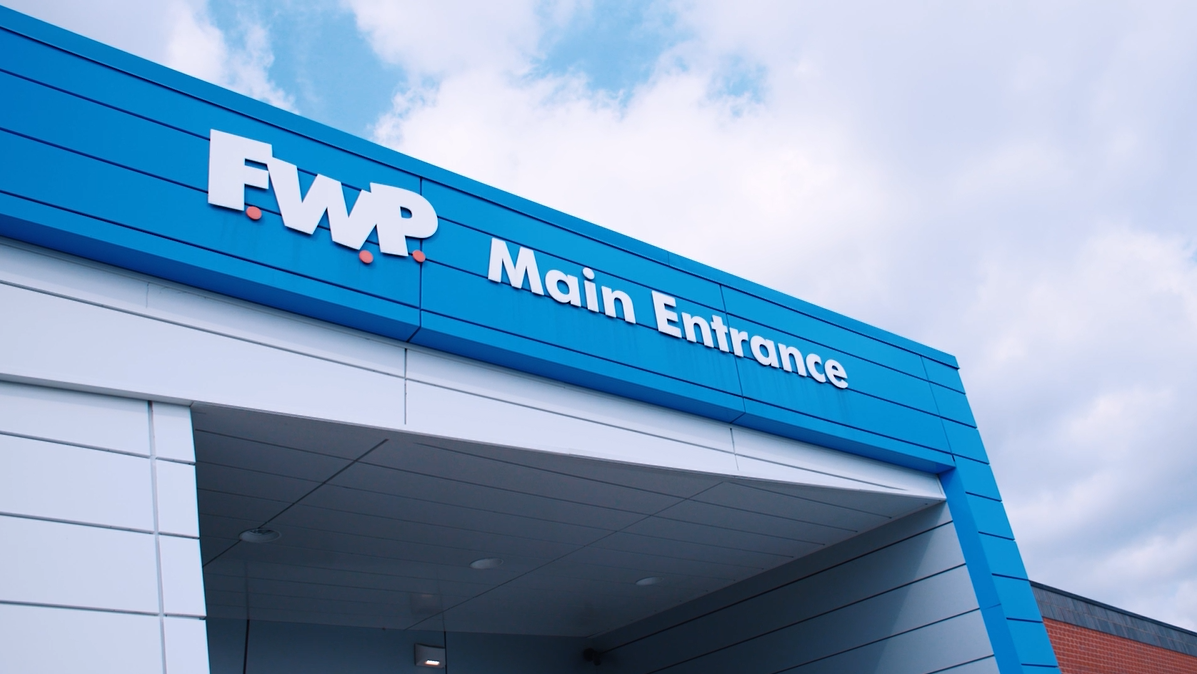 FWP Main Entrance sign on a blue building canopy against a partly cloudy sky