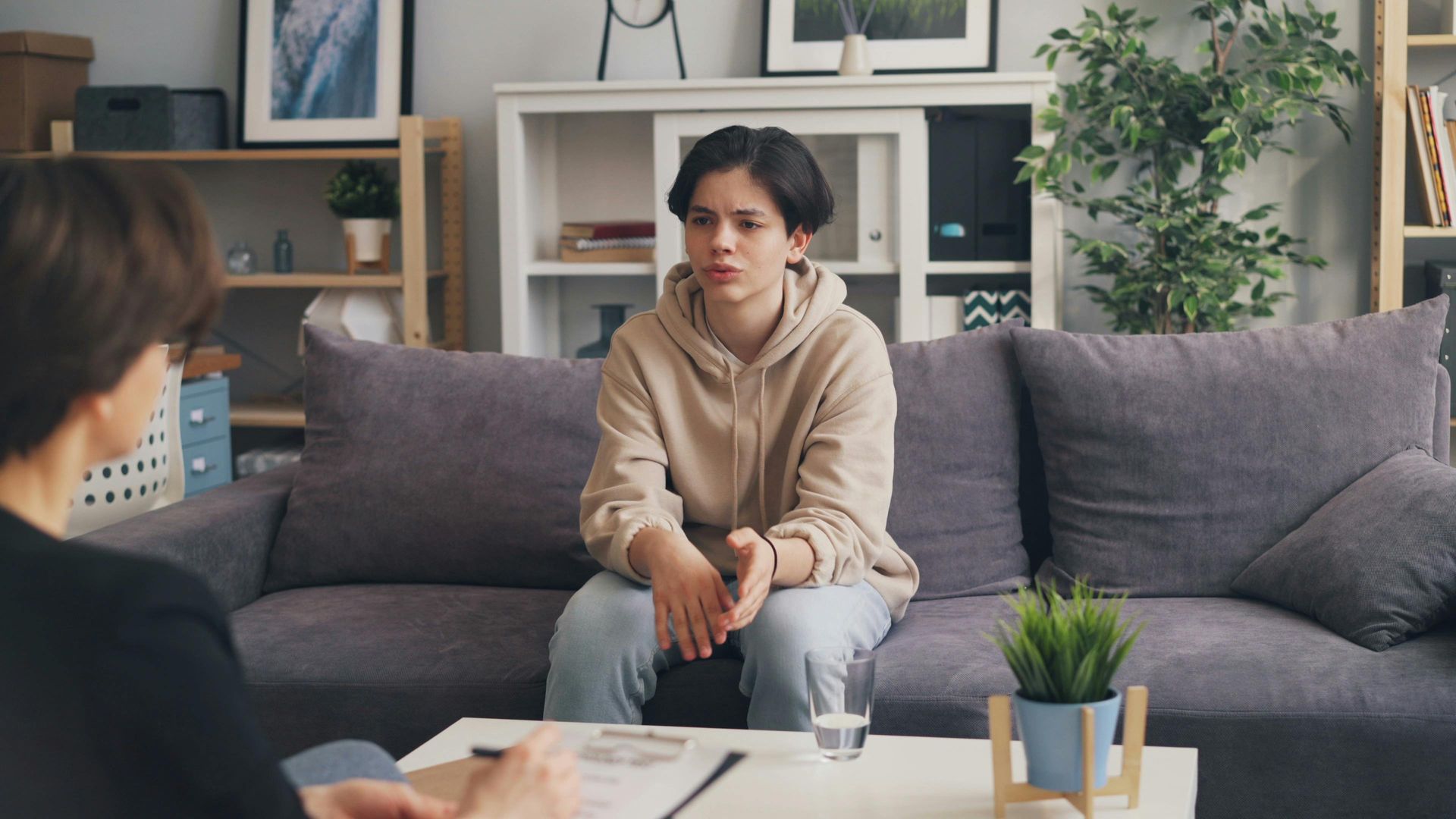 Woman sitting on a gray couch in a living room, listening during a conversation across a coffee table