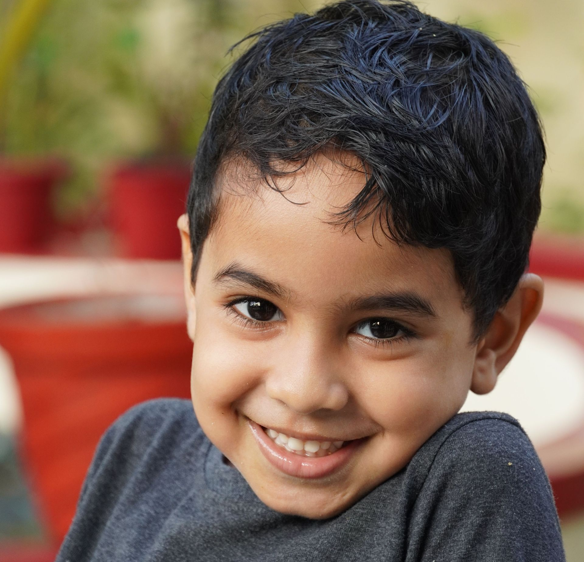 Smiling child in a gray shirt, close-up portrait with a blurred outdoor background
