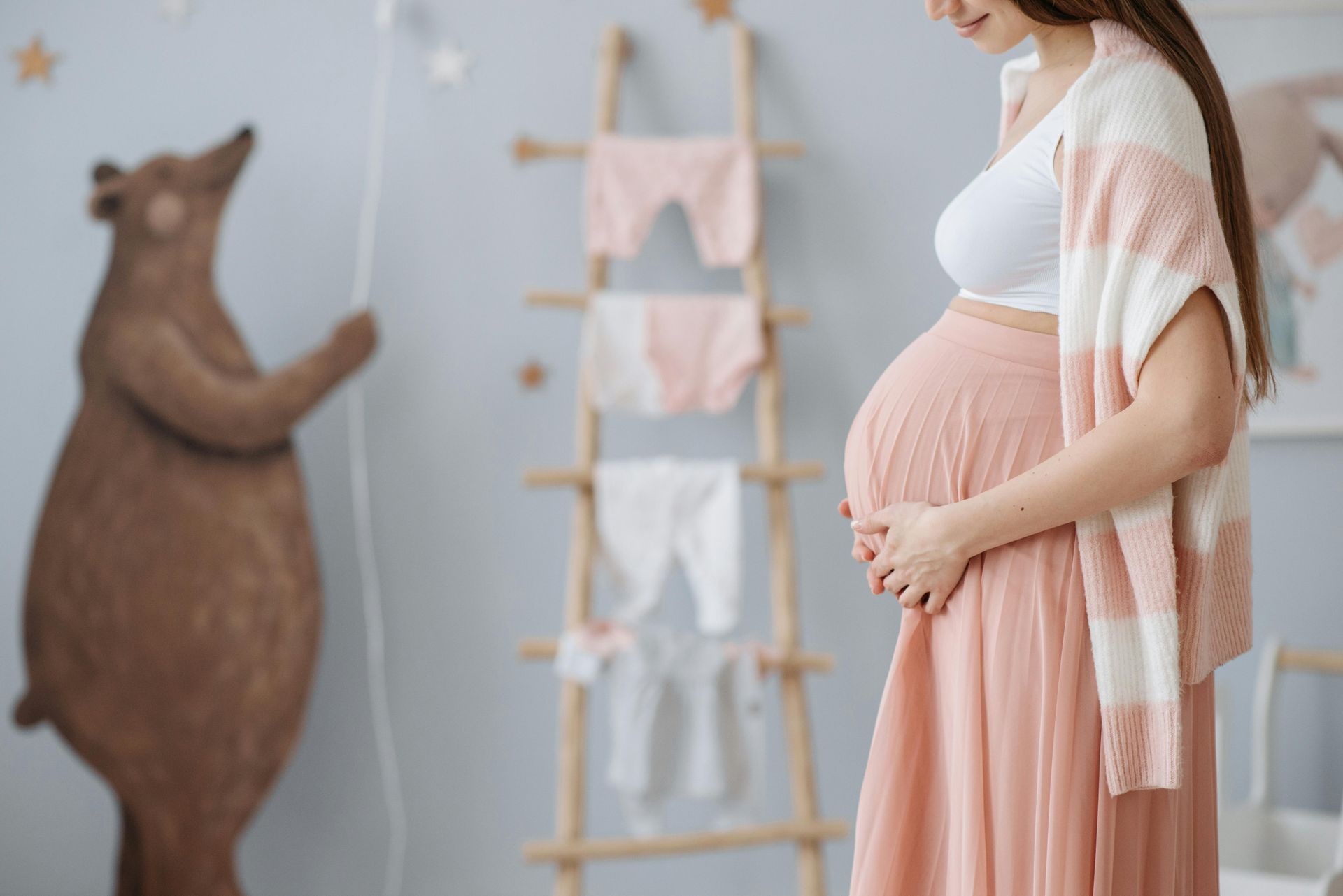 Pregnant woman in a pink dress gently holding her belly in a nursery