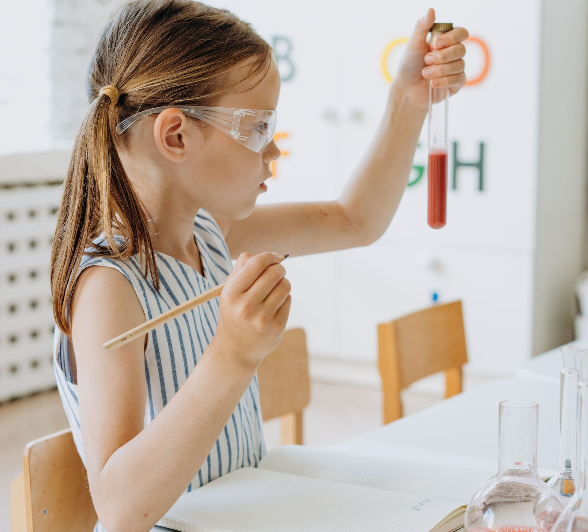 Child wearing safety goggles holds a test tube in a classroom science experiment