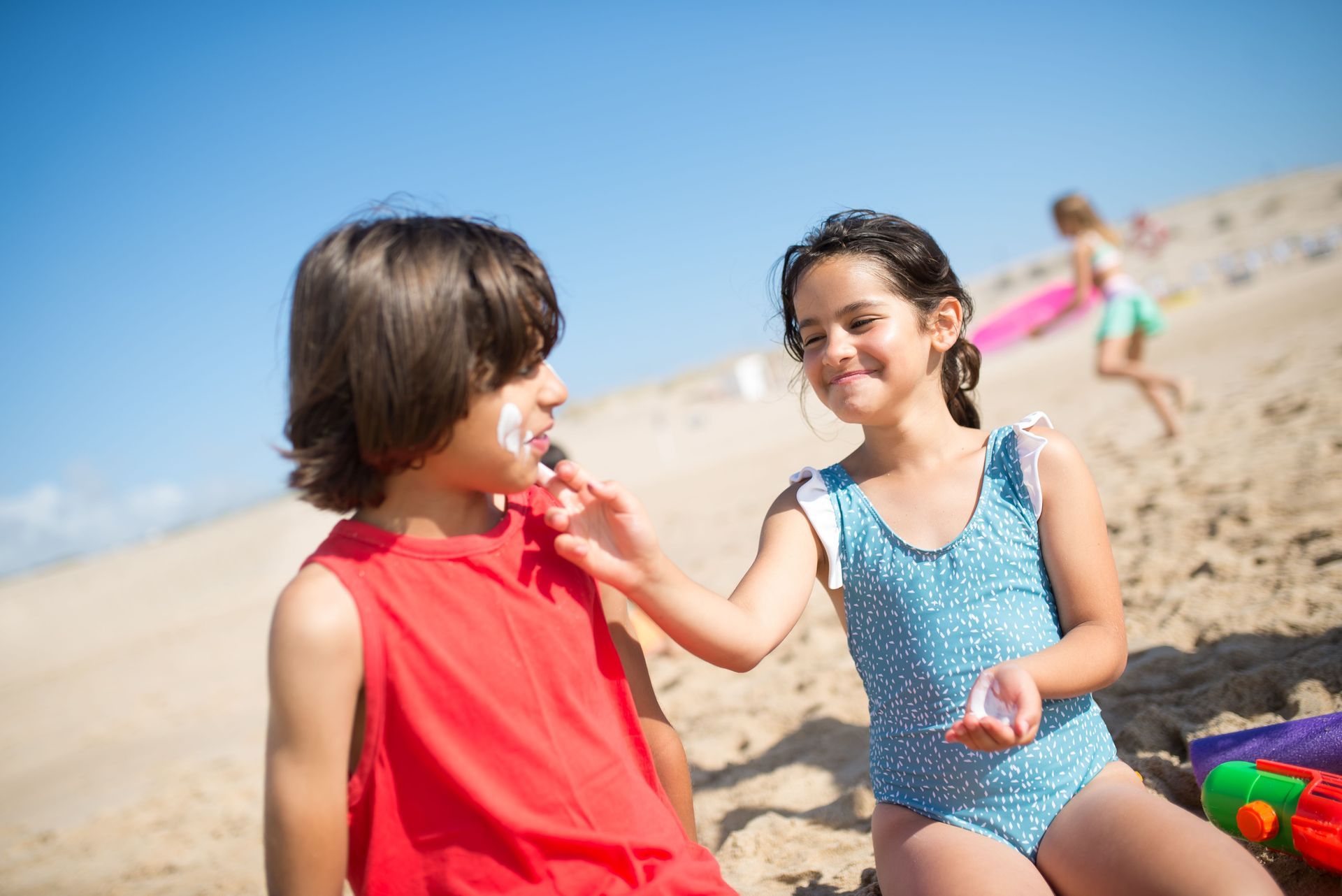 Two children playing at the beach, smiling and holding a red flower in the sand