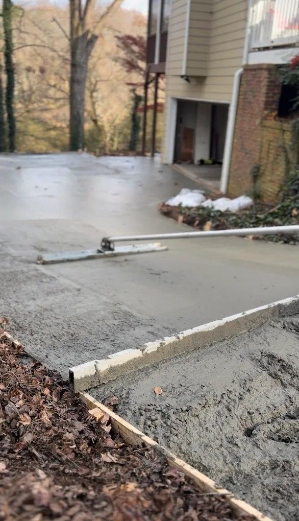 Fresh concrete driveway beside a brick apartment building, with wet surface and work tools visible