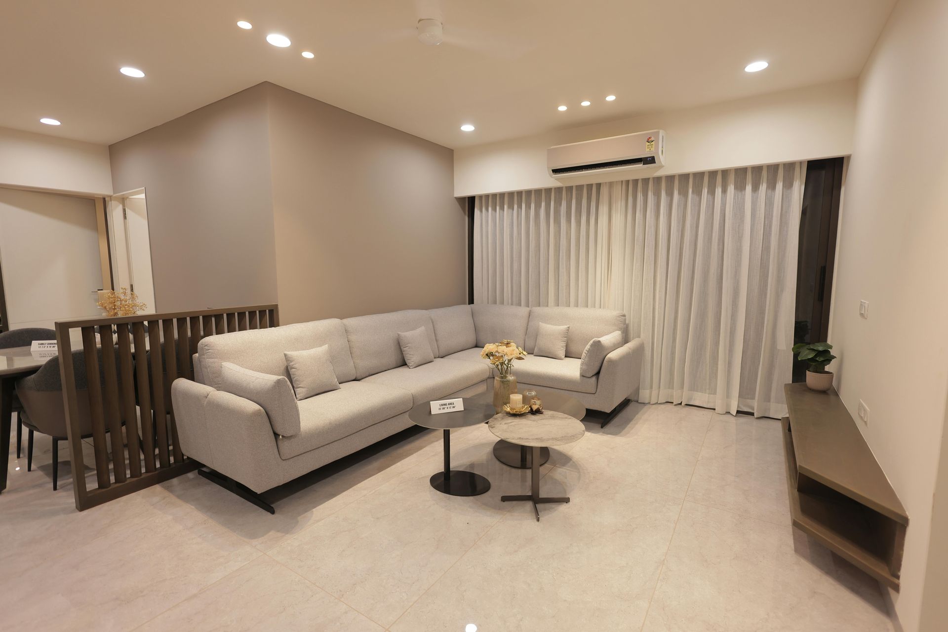 Bright modern living room with beige sectional sofa, coffee tables, curtains, and wall-mounted TV cabinet