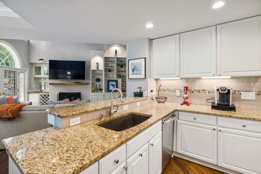 Bright kitchen with white cabinets, granite countertops, and a breakfast bar overlooking a living room.