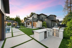 Modern backyard patio with stone walkway, green lawn, and gray house at sunset