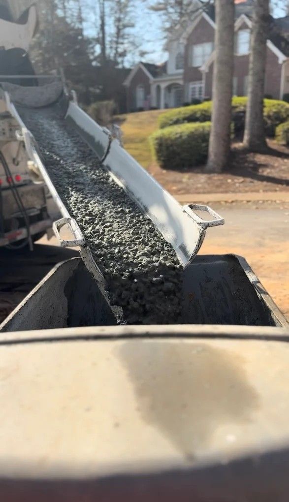 Black gravel spilling from a raised conveyor into a dumpster on a suburban street
