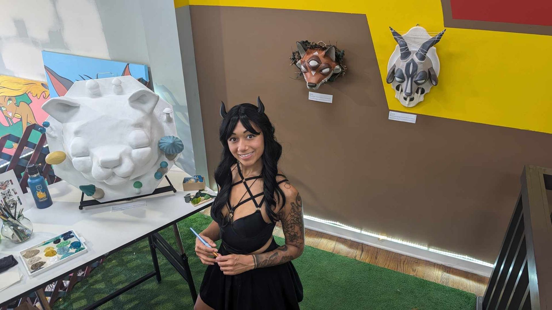 Ashley Alvarado wearing cosplay and standing in front of a table in a room with her scultures.