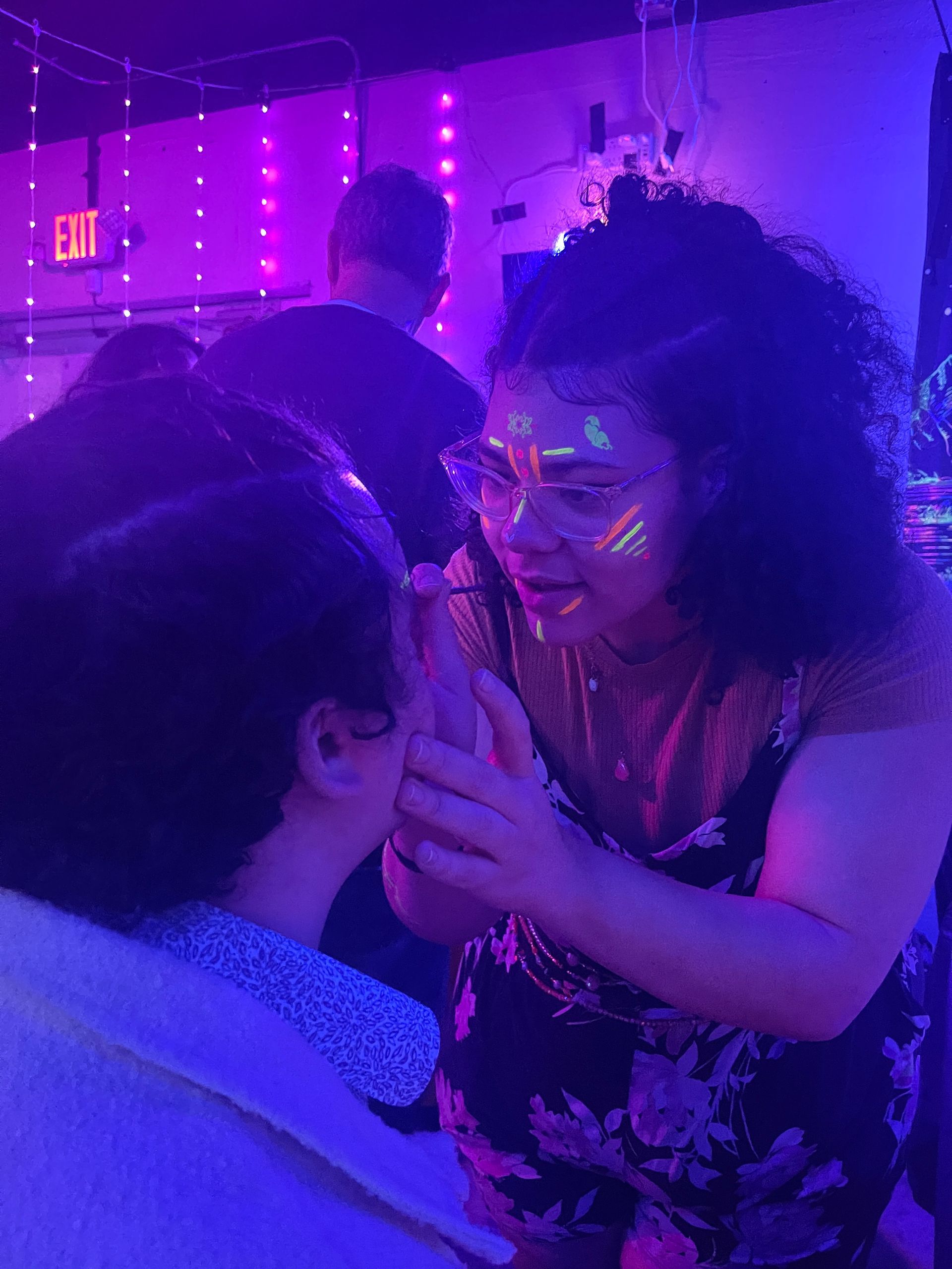 A friend is applying glow in the dark paint to another friend's face.