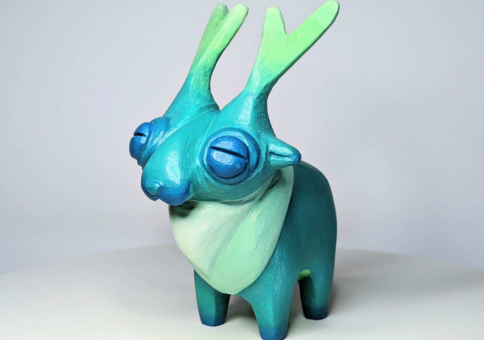 A blue and green figurine of a deer with horns is sitting on a white surface.