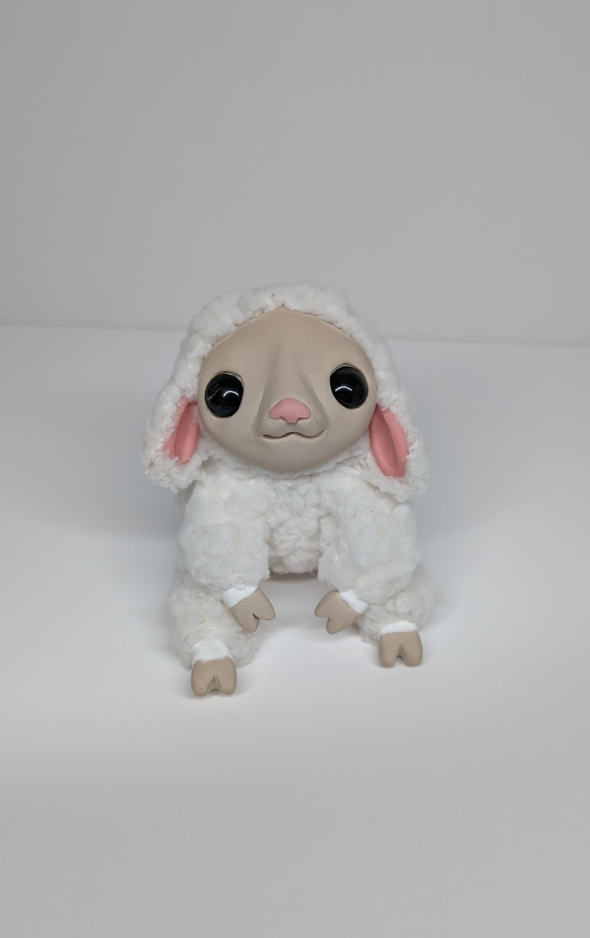 A stuffed sheep is sitting on a white surface.