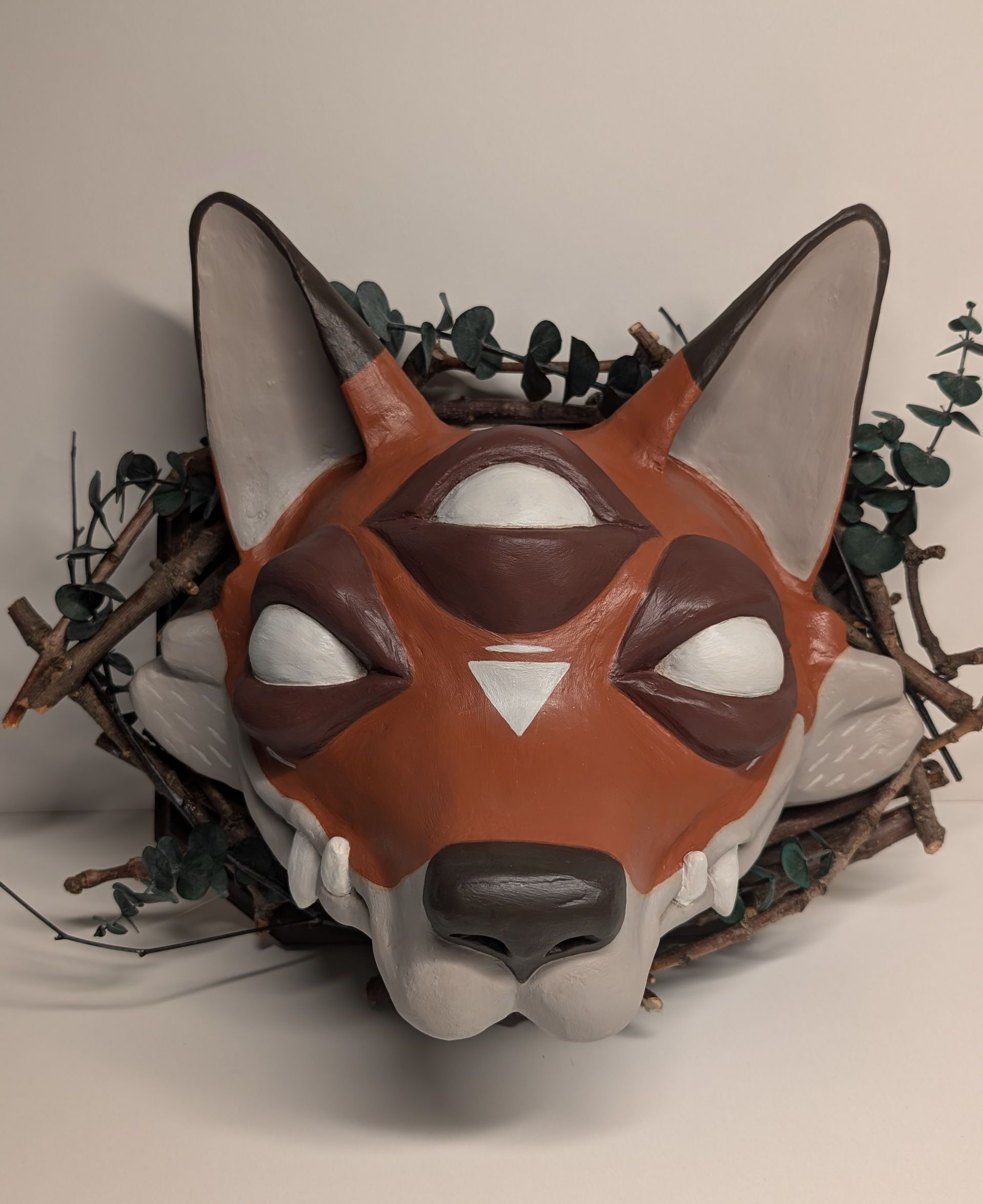 A close up of a fox mask with branches around it