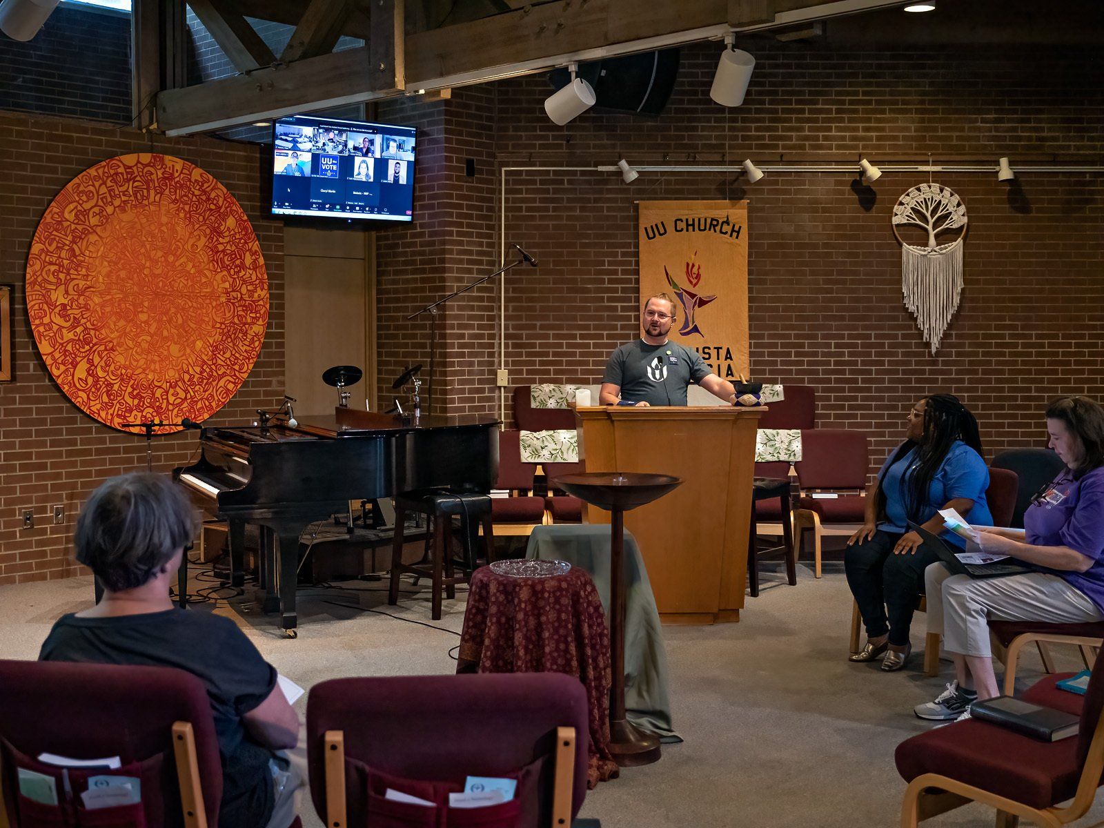 A group of people are sitting in chairs in a room with a man standing at a podium.