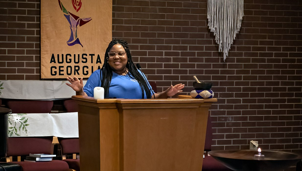 A woman is standing at a podium in front of a brick wall.