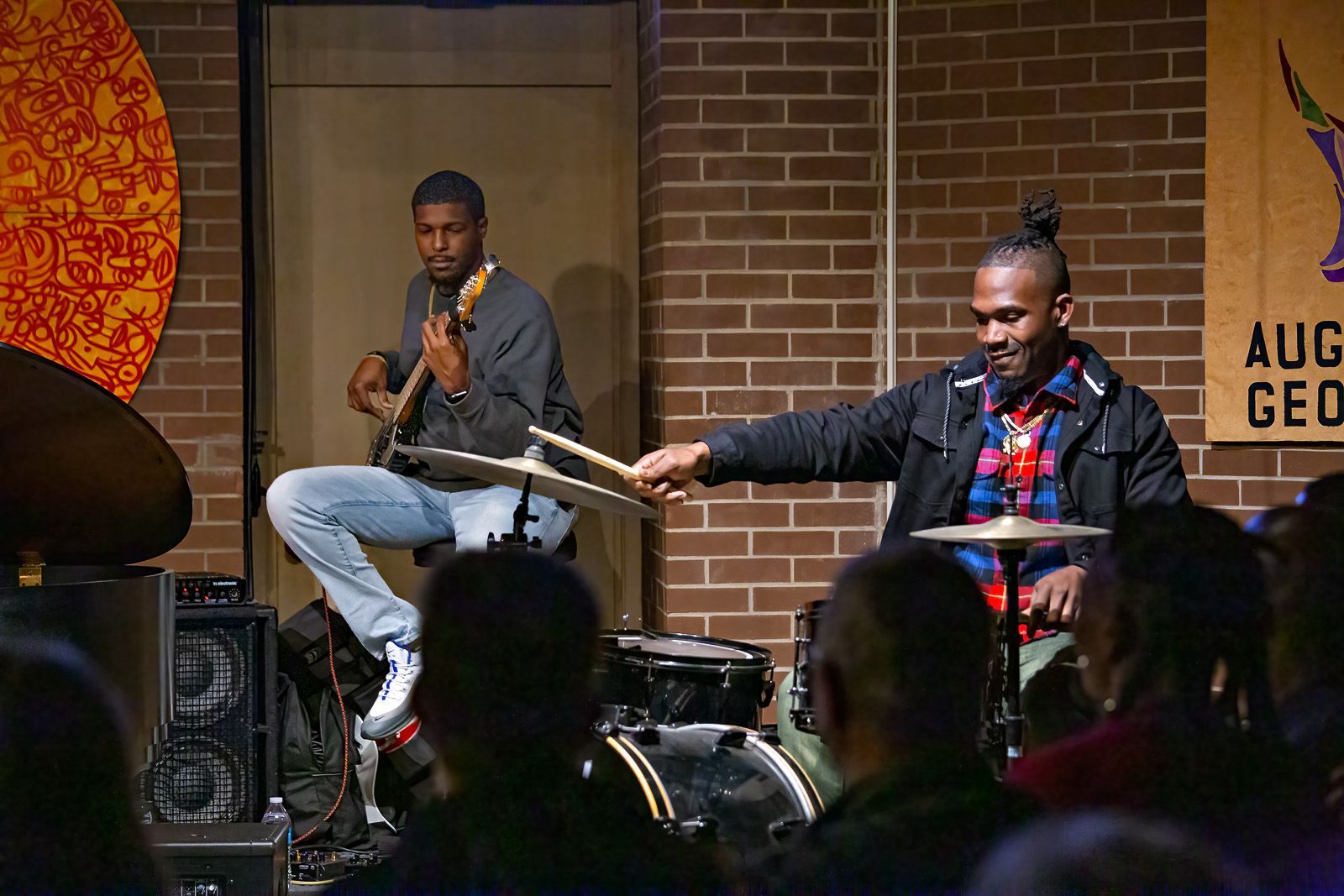 Two men are playing drums and a guitar on stage.