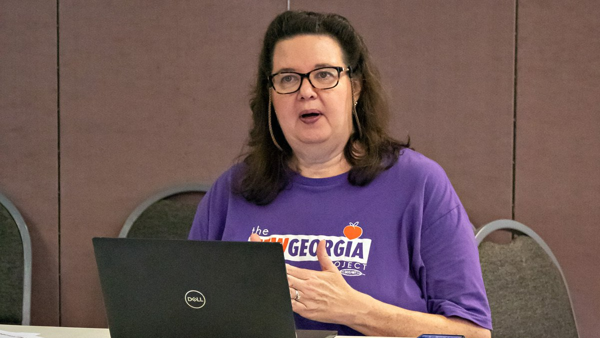 A woman in a purple shirt is sitting at a table with a laptop.