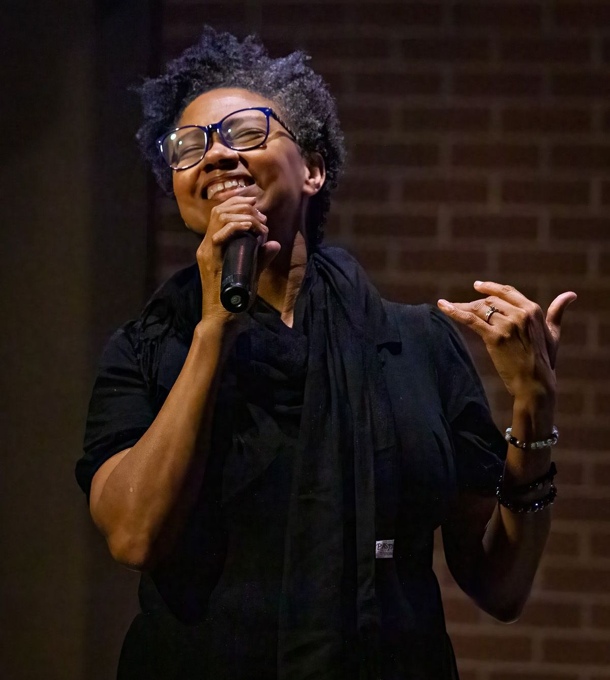 A woman wearing glasses is singing into a microphone