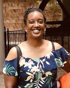 A woman in a blue floral off the shoulder top is smiling.