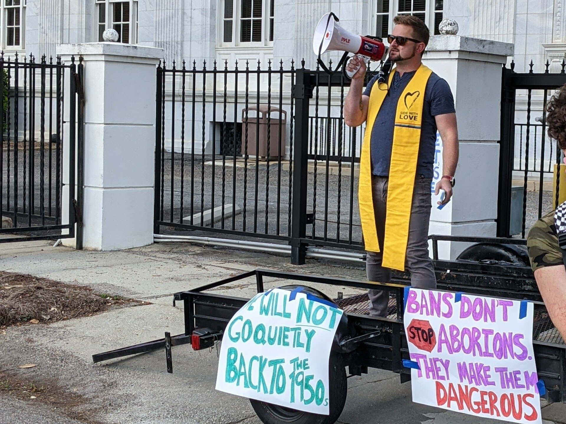 A man is holding a megaphone while standing on a trailer with signs on it.