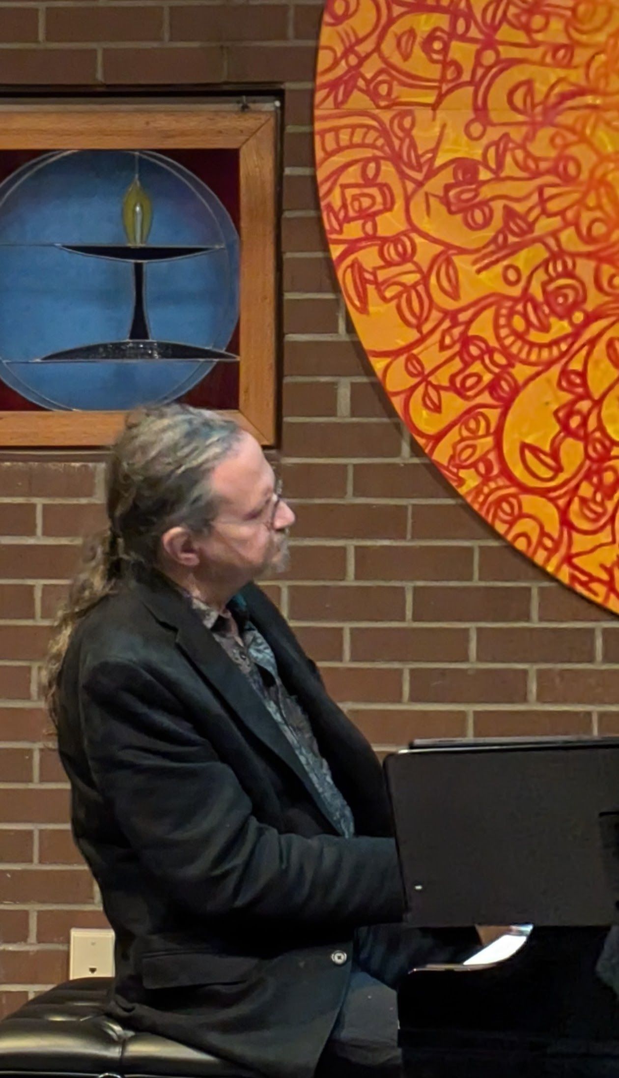 A man in a suit is playing a piano in front of a brick wall.