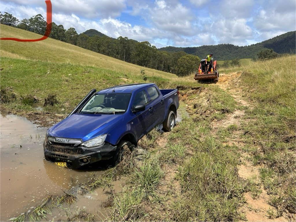 A Blue Truck Is Stuck in The Mud on A Dirt Road — Twin Lakes Towing & Recovery in Warners Bay, NSW
