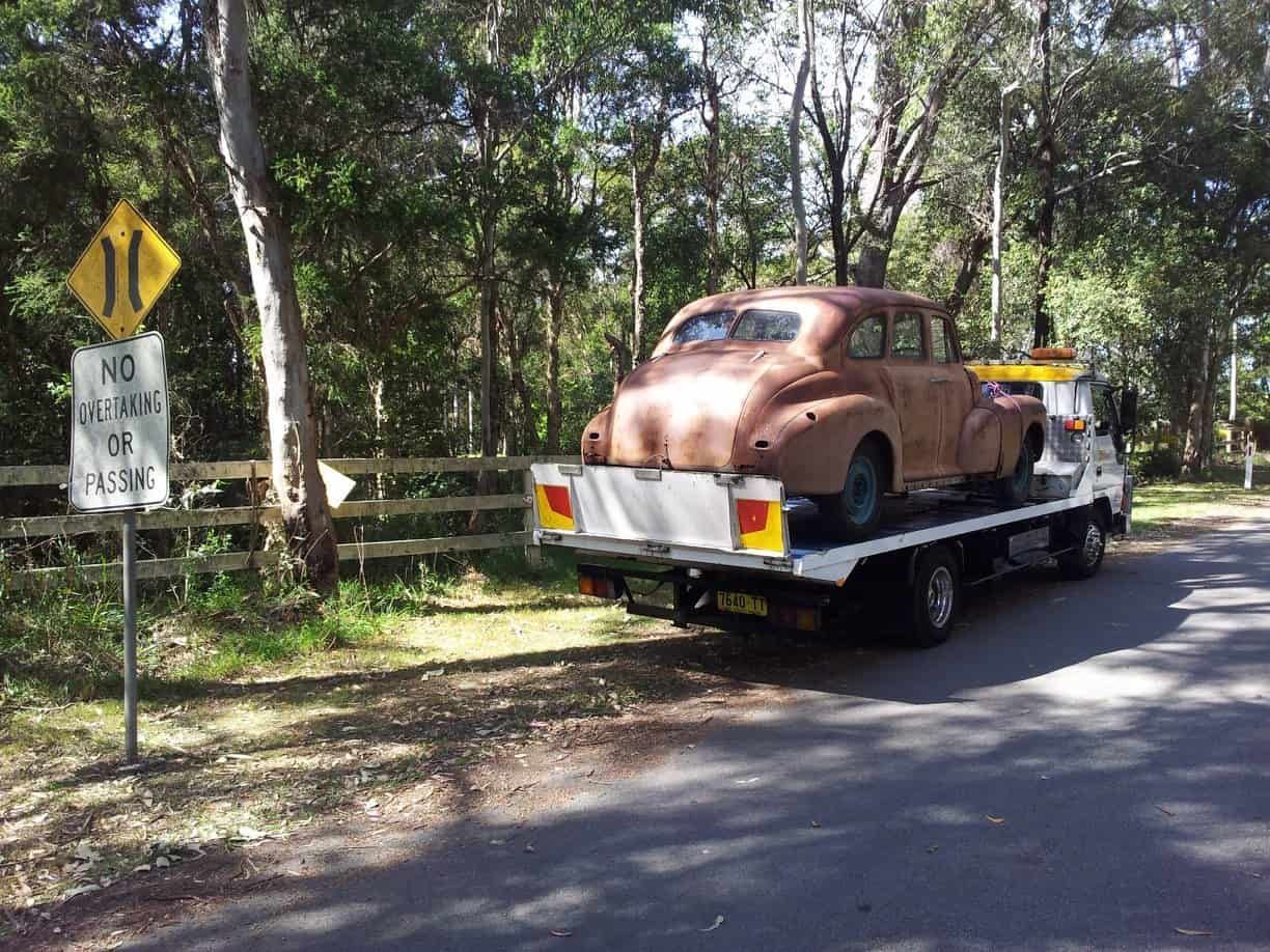 An Old Car Is Being Towed Down a Road by A Tow Truck — Twin Lakes Towing & Recovery in Toukley, NSW