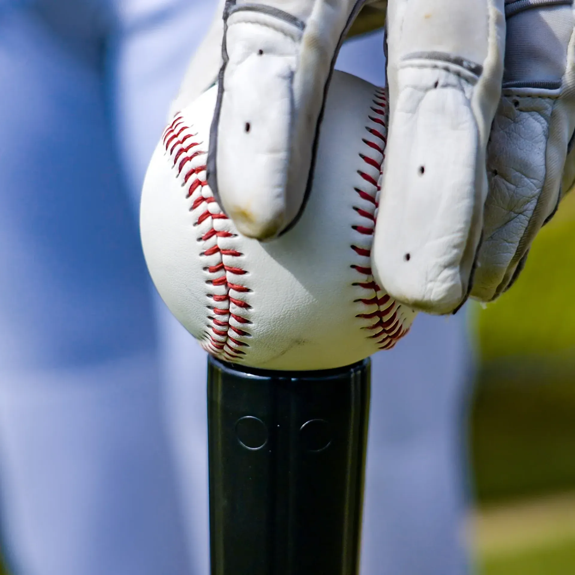 A person wearing white gloves is holding a baseball on a bat