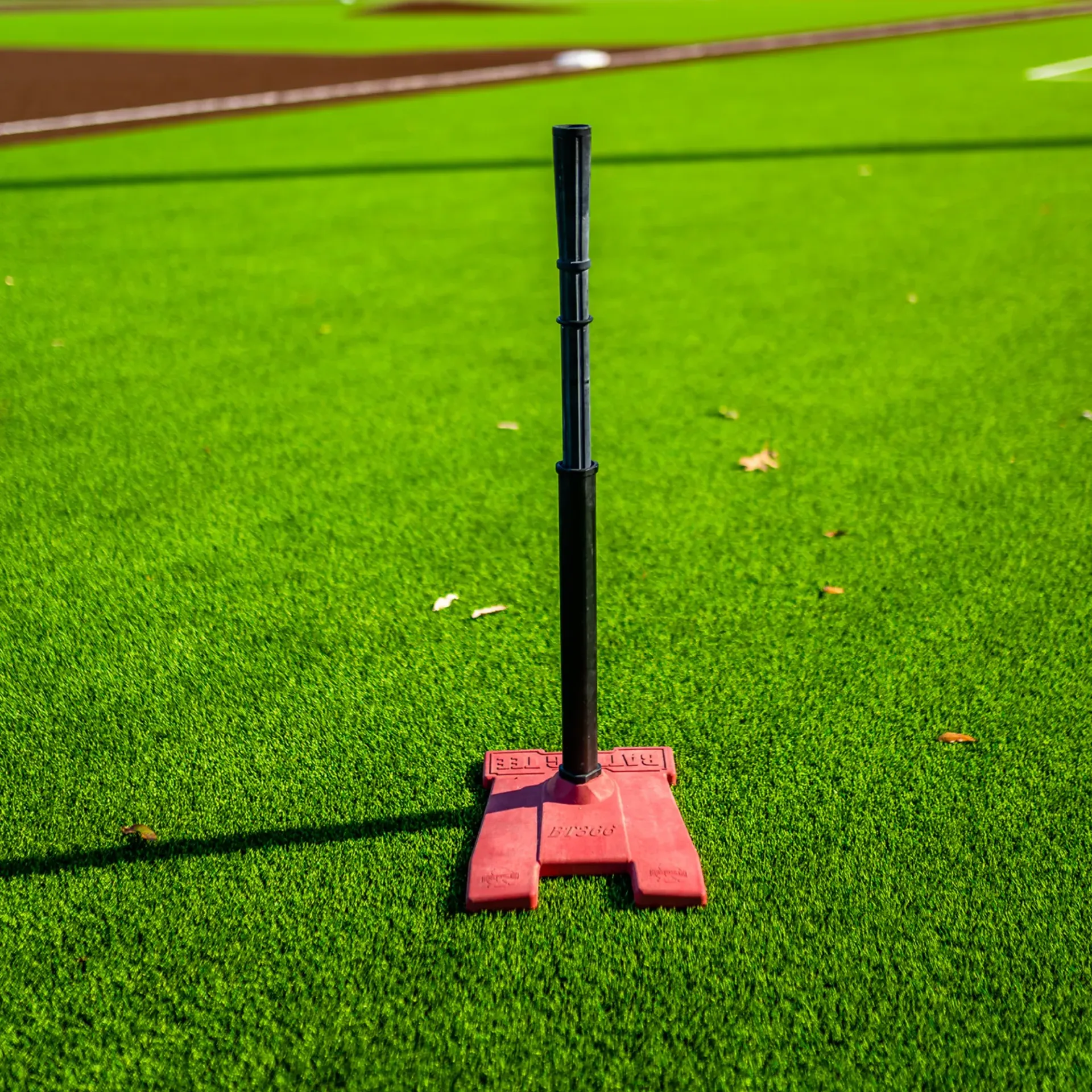 A baseball bat is sitting on top of a red base on a baseball field.