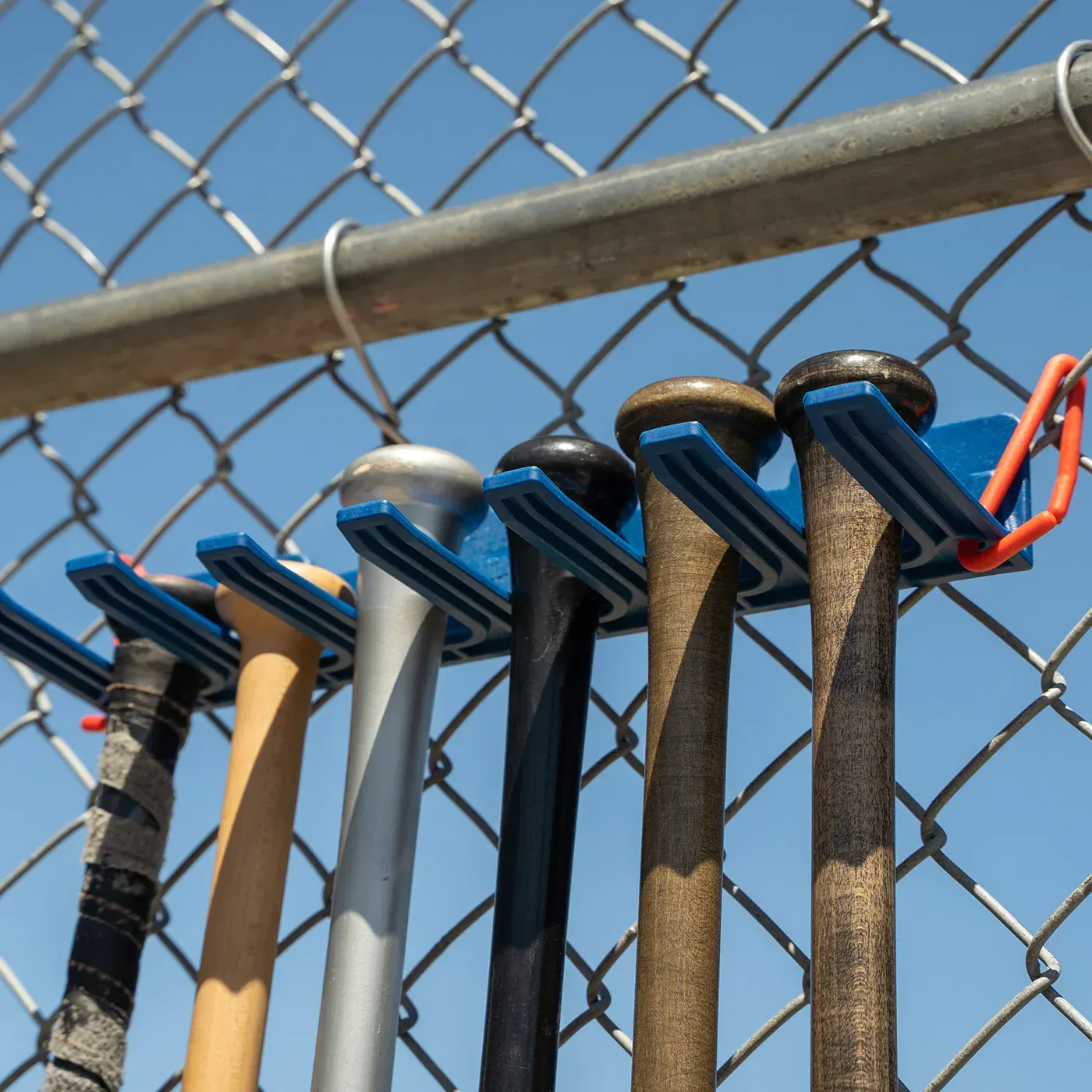 A bunch of baseball bats hanging on a chain link fence