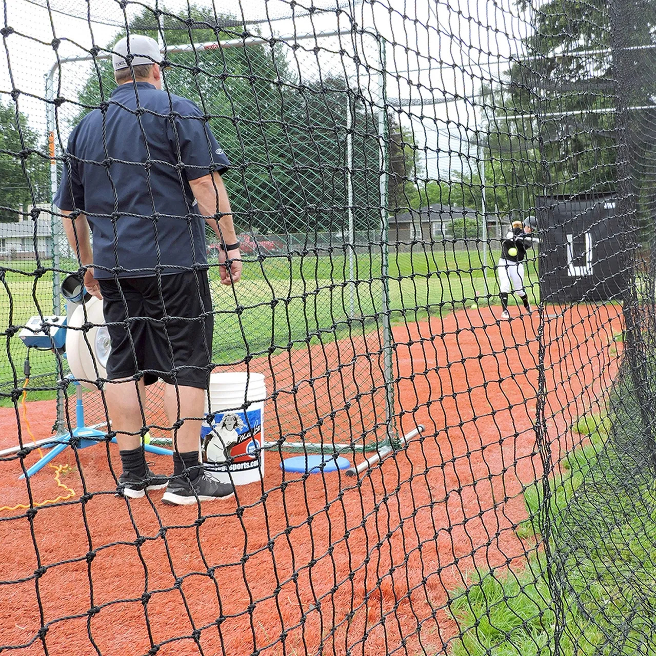 A man is standing behind a net on a baseball field