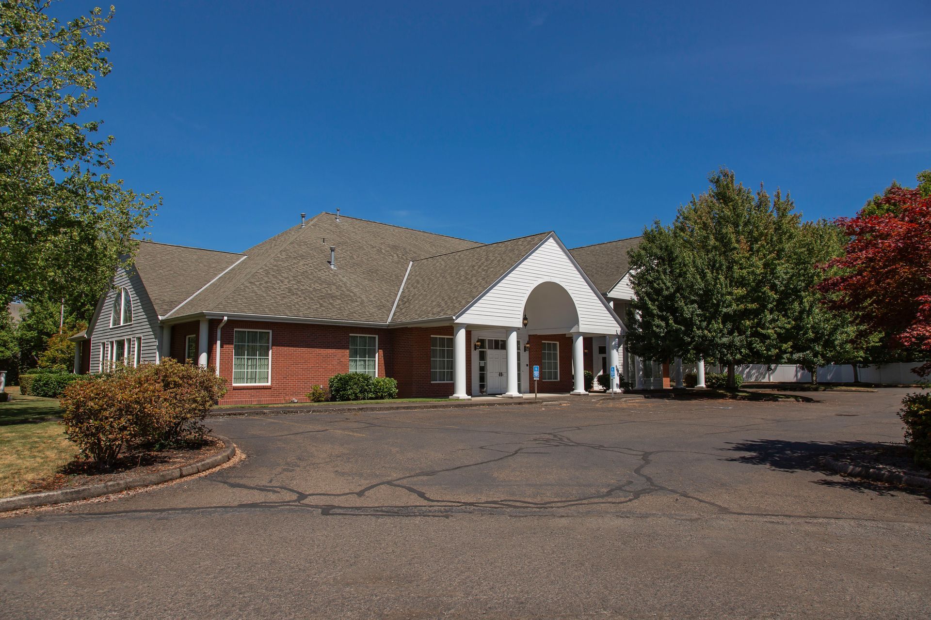 Red brick building with white pillars and a dark driveway under a blue sky.