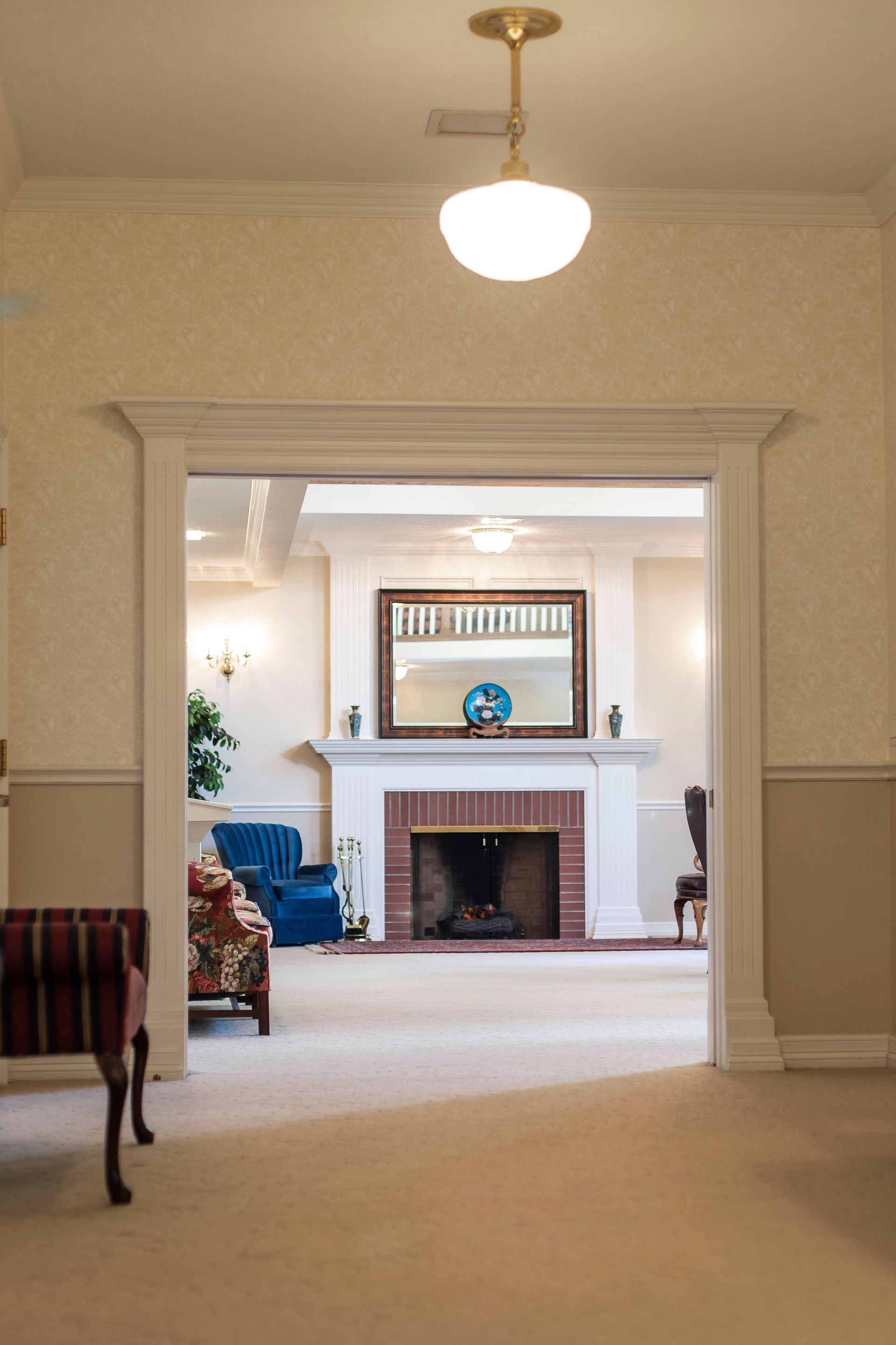 Interior view through a doorway into a room with a fireplace, mirror, chairs, and a light fixture.