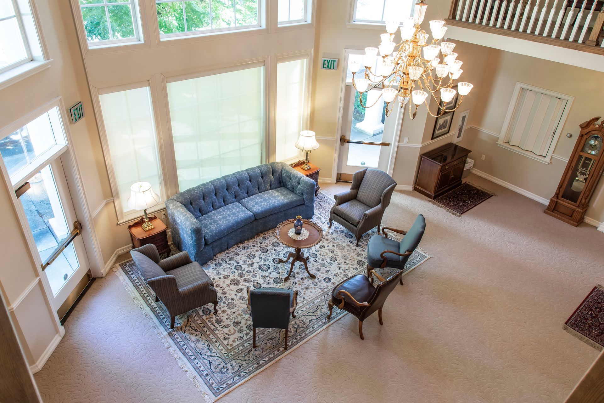 Lobby with blue sofa, armchairs, chandelier, and carpet; windows on multiple walls.