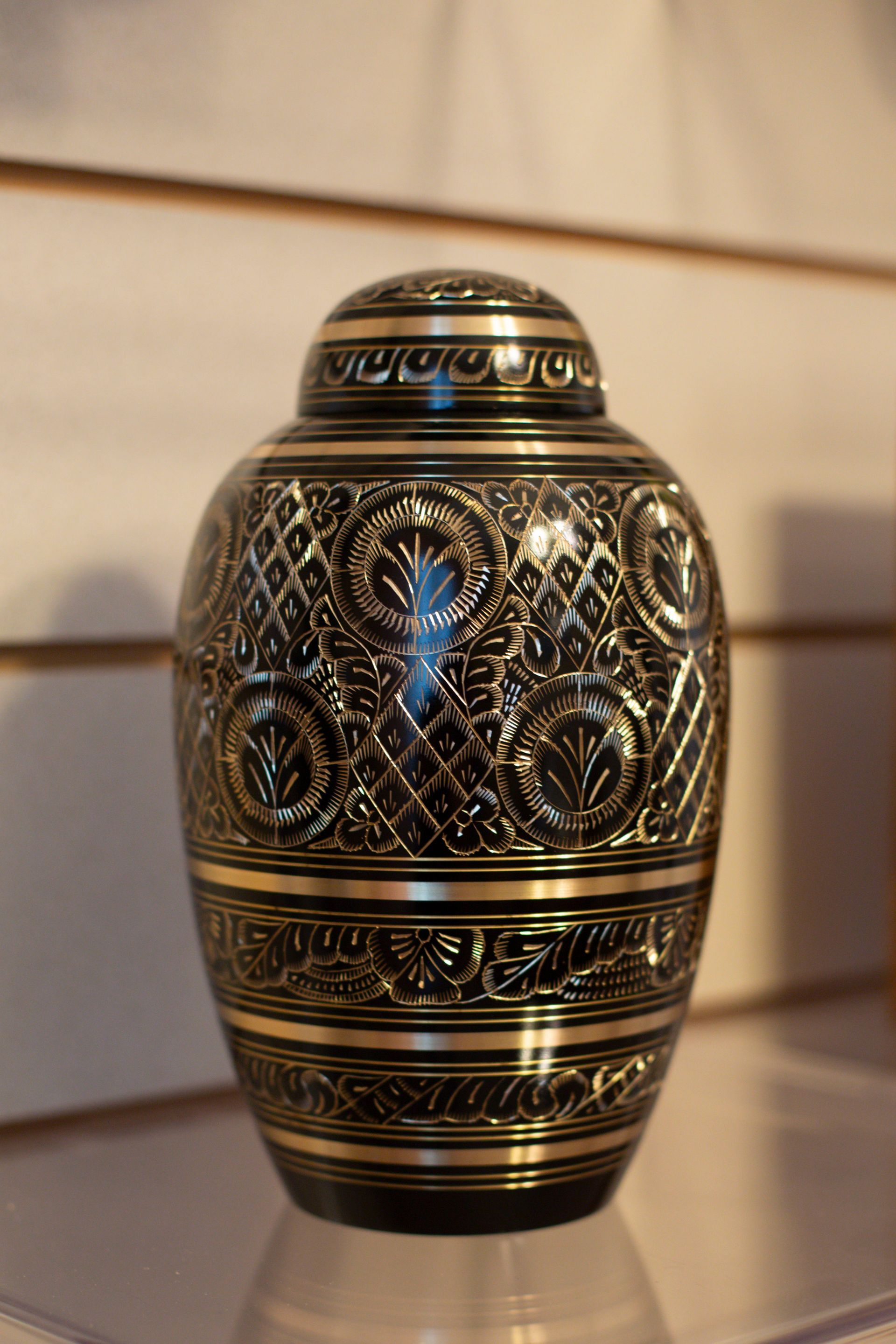 Black and gold urn with ornate floral and geometric patterns, with a matching lid.