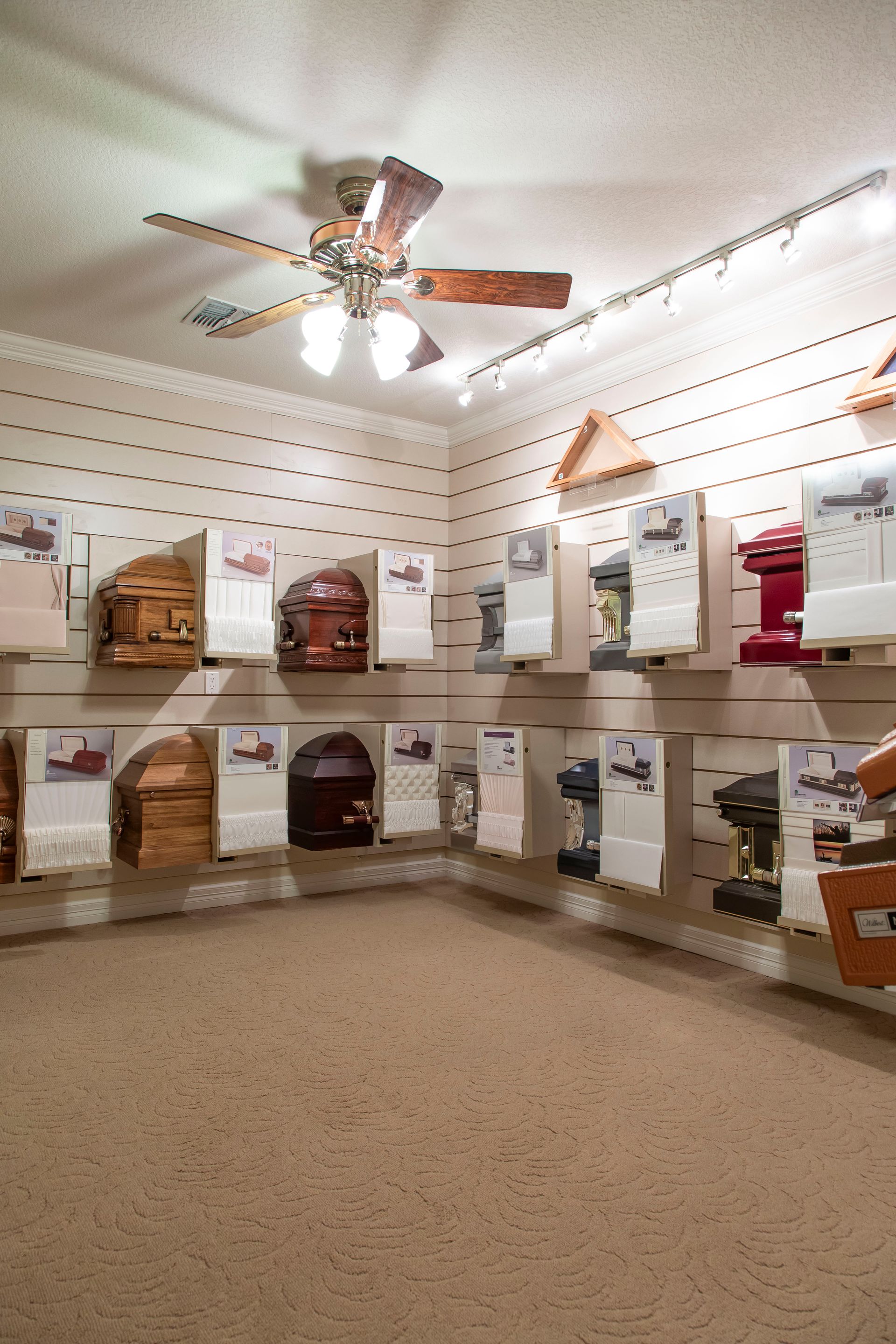 A room displaying various caskets, with a ceiling fan overhead.