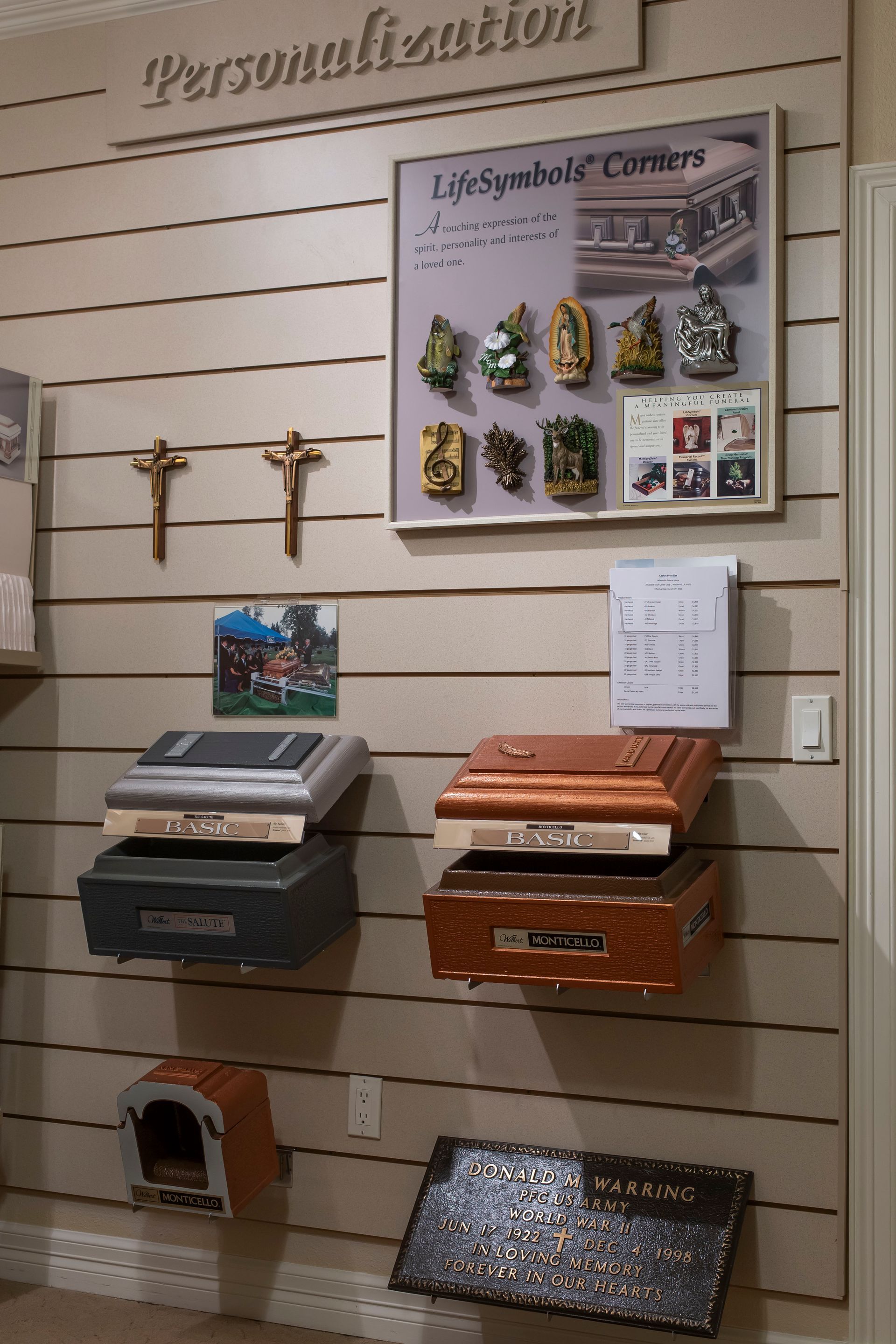 Wall display of personalized urns, crosses, and life-symbol plaques in a funeral home. Beige and brown tones.