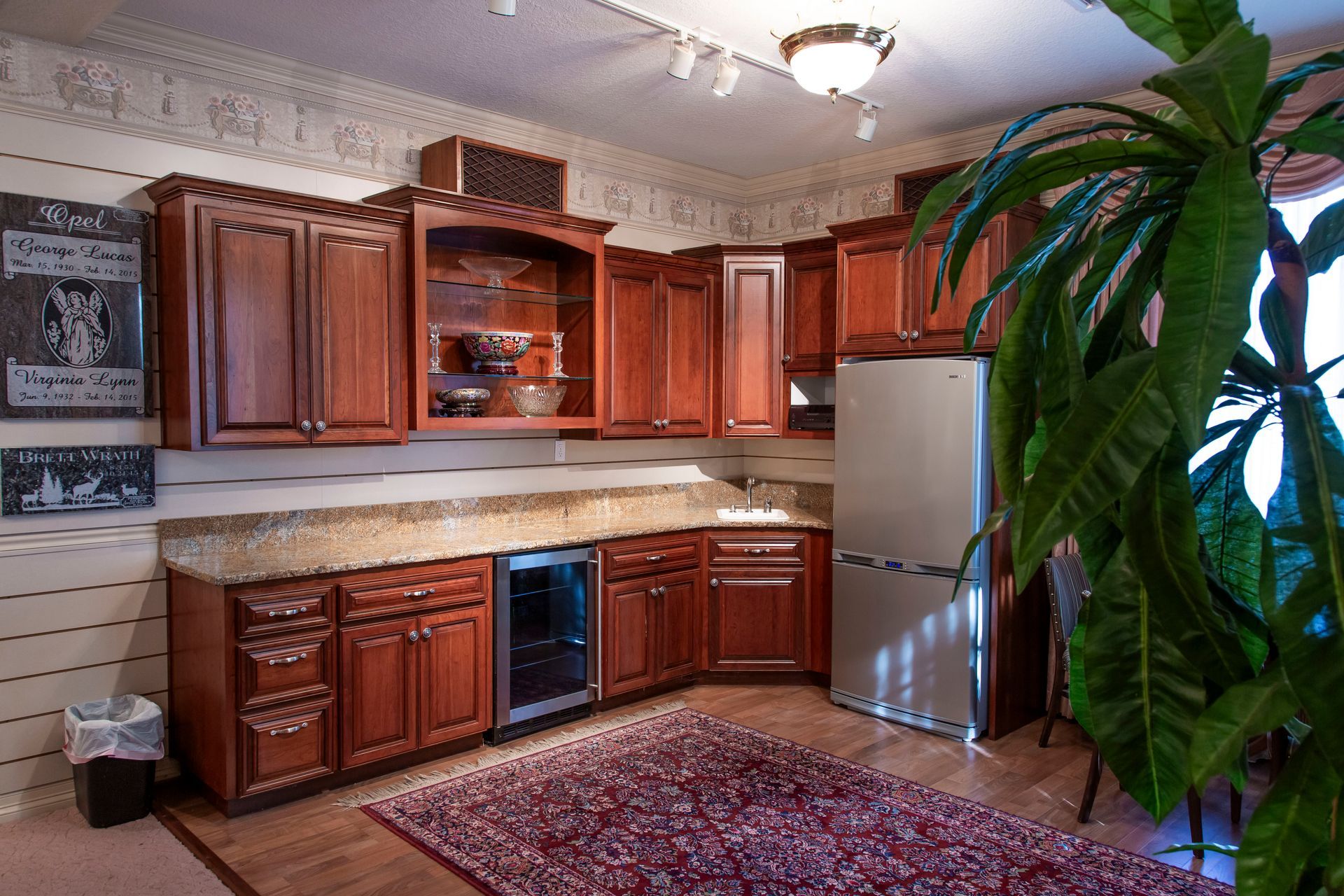 Kitchen with wooden cabinets, stainless steel refrigerator, wine cooler, and a large plant.