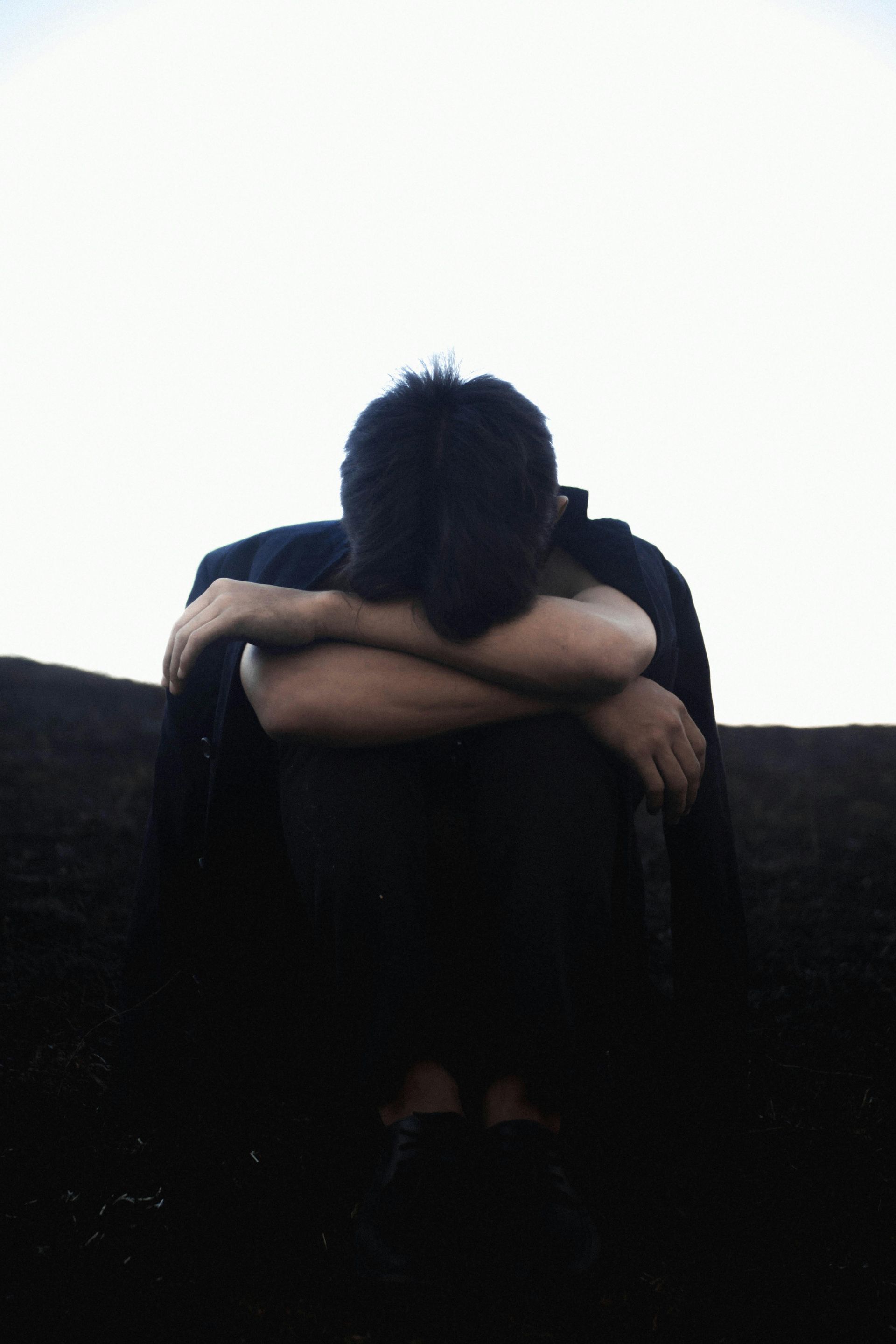 Person sitting with head down and arms crossed on a dark ledge against a bright background