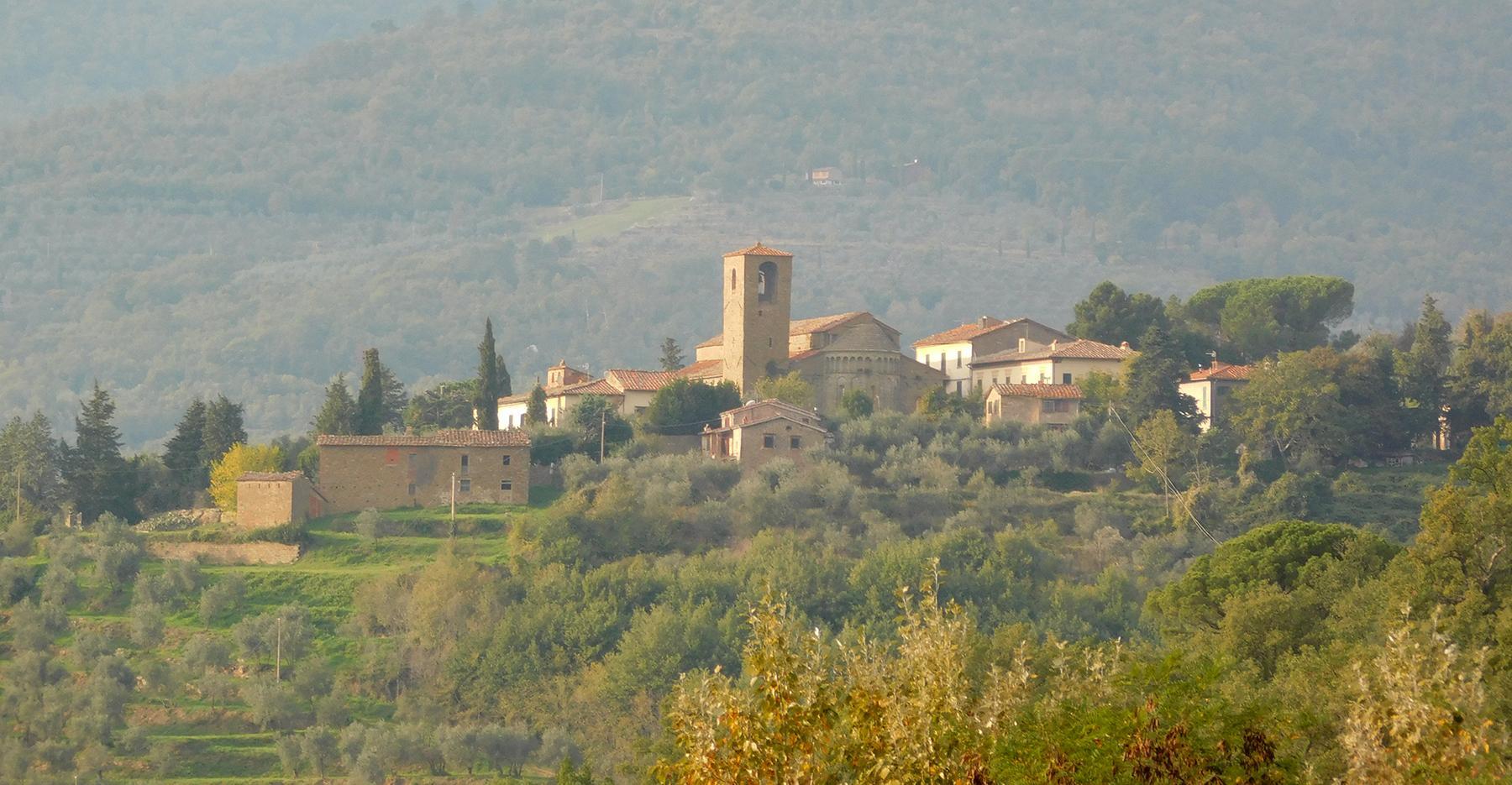 Hilltop village with stone buildings, a church tower, and olive trees.