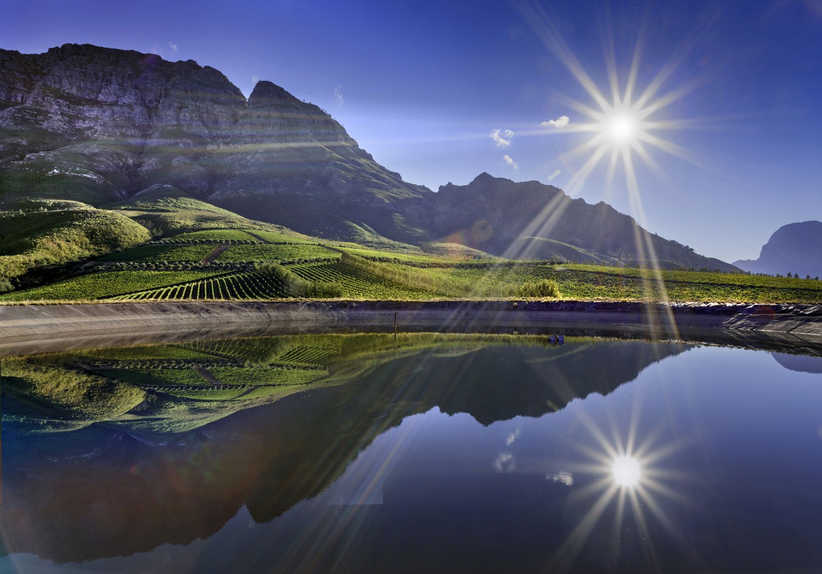 Mountains and vineyards reflected in a still body of water, at Tokara winery.