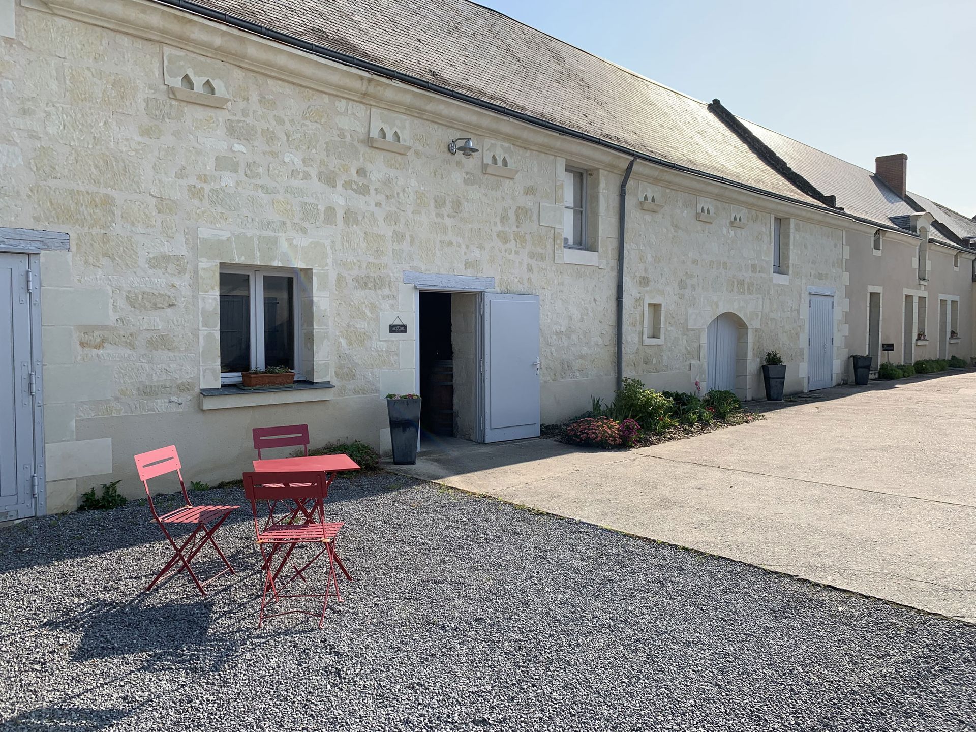 Exterior of Domaine Olga Raffault building with open doors, red table, and chairs on gravel.
