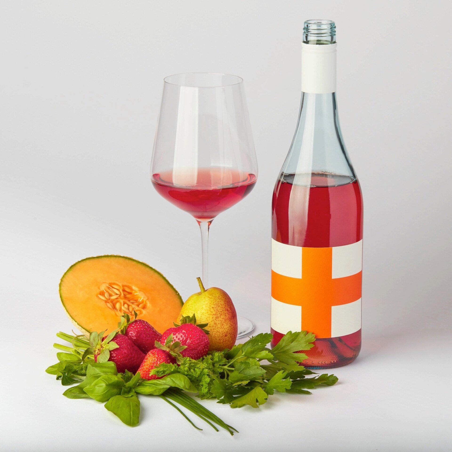 Bottle and glass of red wine with fruit and herbs.