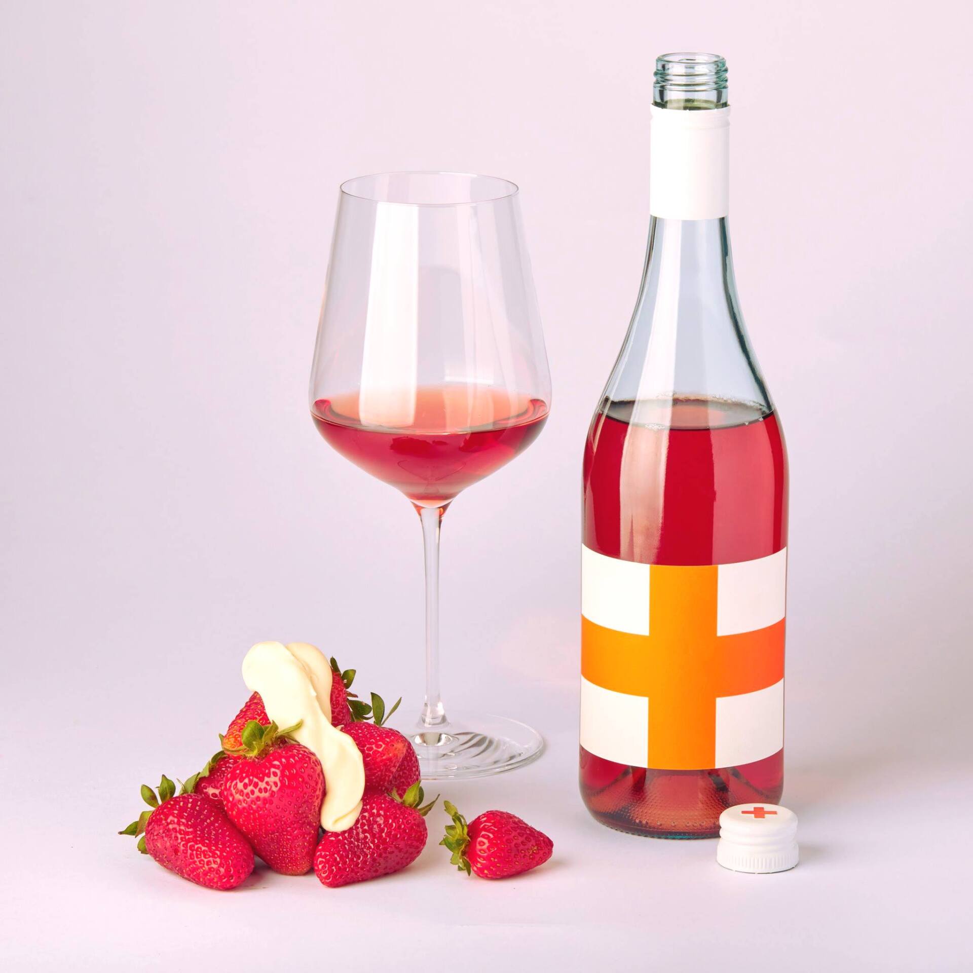 Bottle and glass of pink wine, strawberries with cream, white background, orange and white label.
