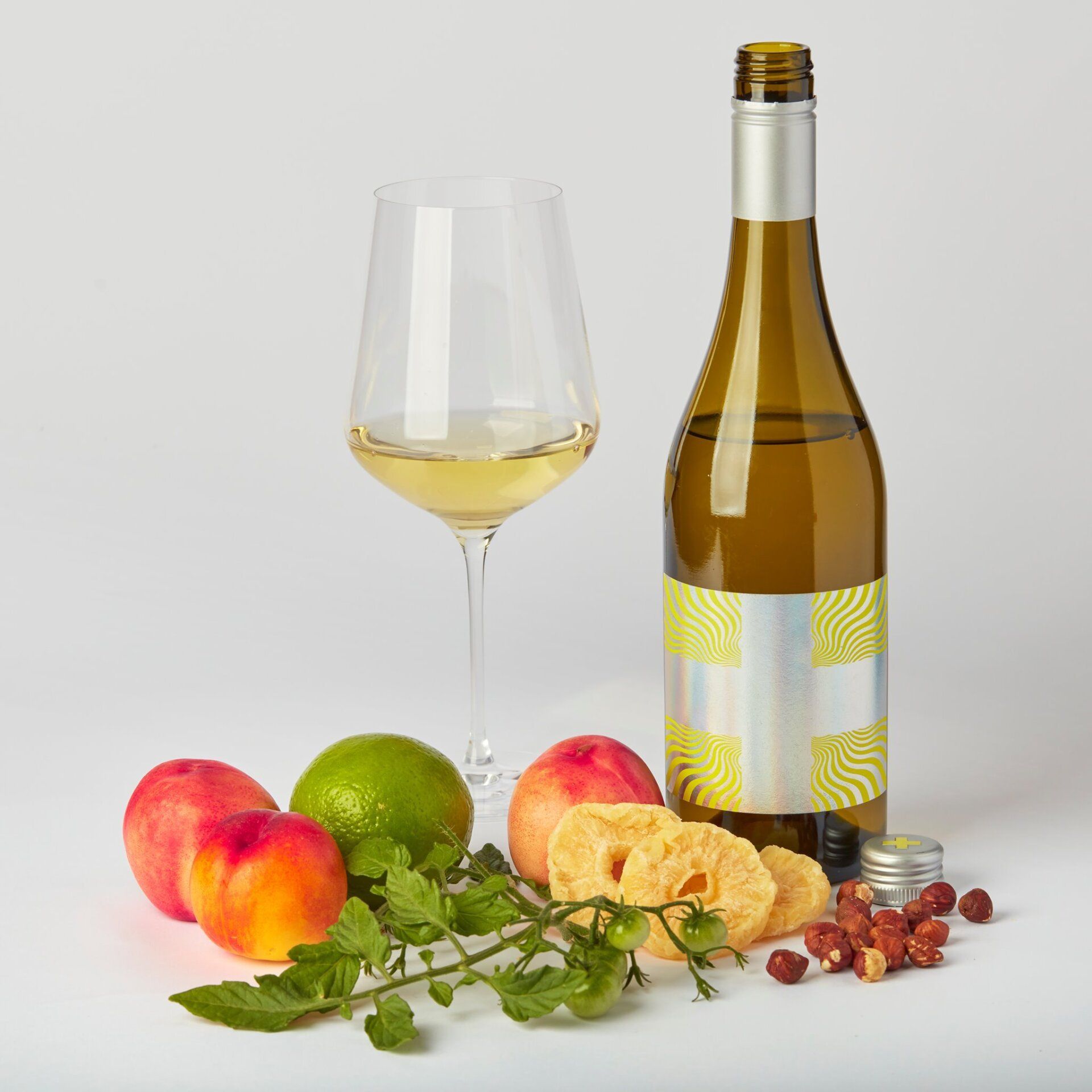White wine bottle and glass with fruit and nuts on a white background.