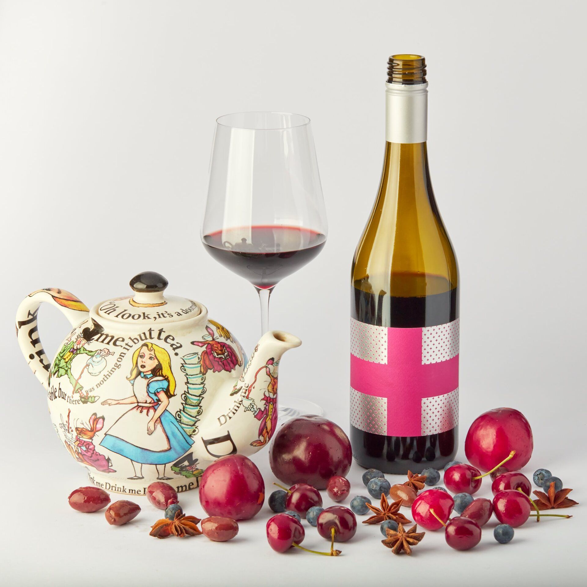 An image with a teapot, red wine glass, Save our Souls wine bottle, and fruit on white.