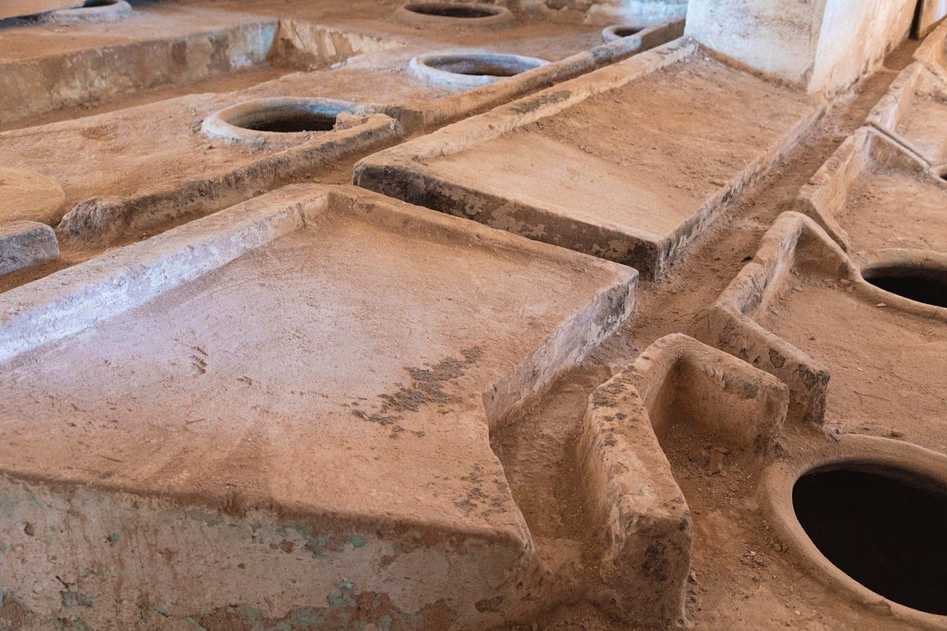 Stone vats and troughs in an ancient, earthen-floored room, likely used for food or liquid processing.