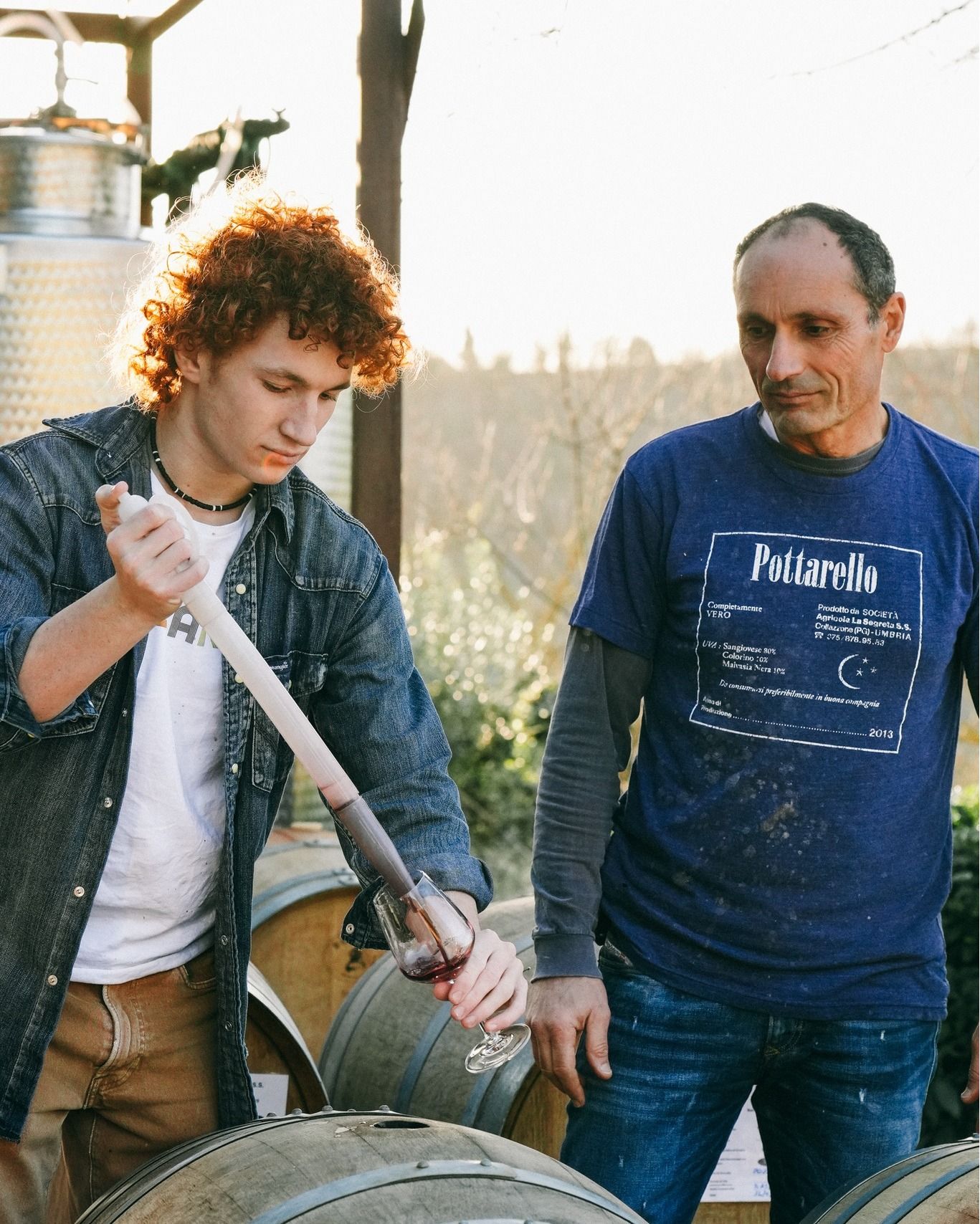 Two winemakers at Agri Segretum taste wine from a barrel, pouring it into a glass.