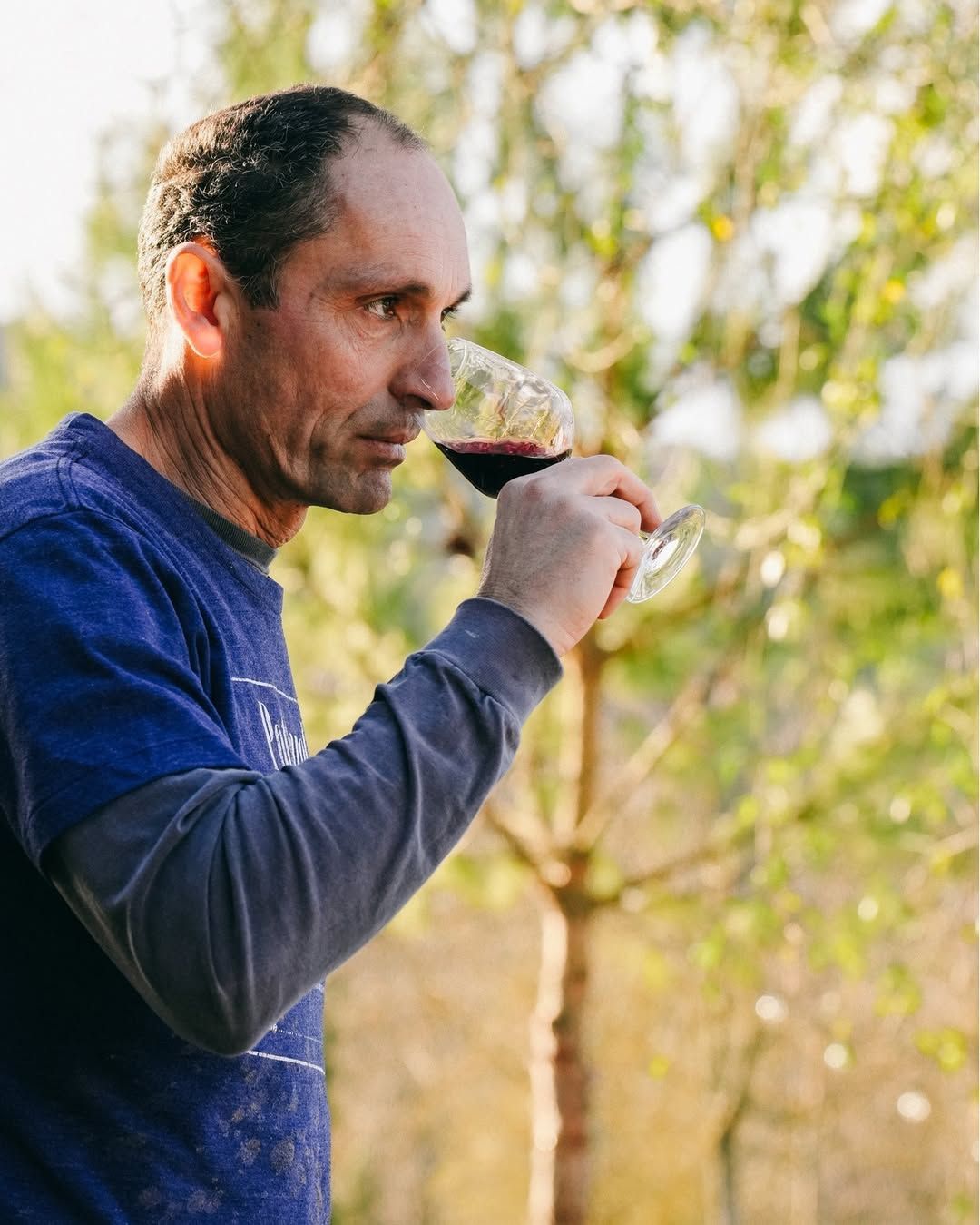 A winemaker at Agri Segretum tastes wine outdoors among trees and vines.