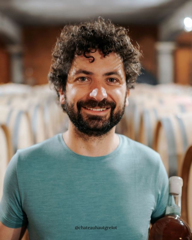 Winemaker of Château Haut Grelot standing in the barrel cellar holding a bottle.