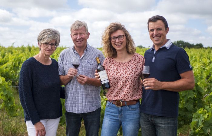 Four people in vineyard, holding wine glasses and a bottle, at Château Saint Hilaire